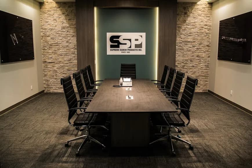 Modern conference room with dark table, black chairs, brick accent walls, teal feature wall with logo, and professional lighting design by Mariama Agi.