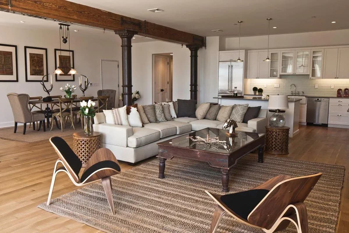 Open-concept living and dining space with cream sectional, wooden beams, and modern furnishings designed by Marie Burgos.