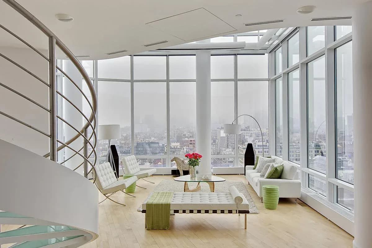 Modern penthouse living room with floor-to-ceiling city views, spiral staircase, minimalist furniture, and natural wood flooring by Marie Burgos.