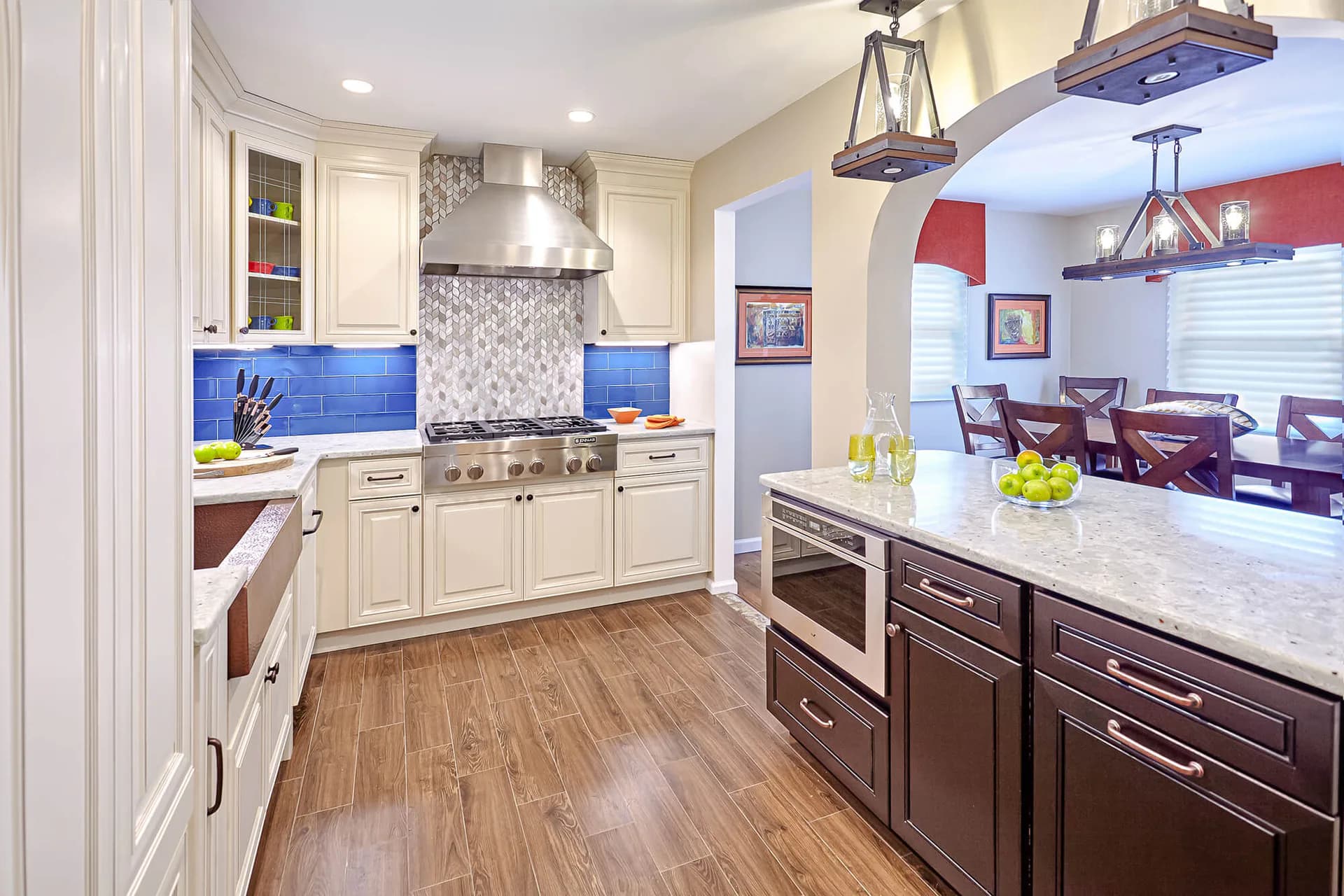 Modern kitchen with cream cabinetry, blue backsplash, wood floors, and a dark island with marble countertop by Marilyn Ajose.