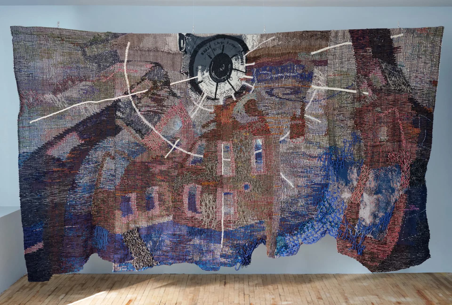 Large-scale textile wall installation featuring abstract layered imagery with architectural elements, geometric patterns, and a prominent circular mechanical component, by Maris Van Vlack.