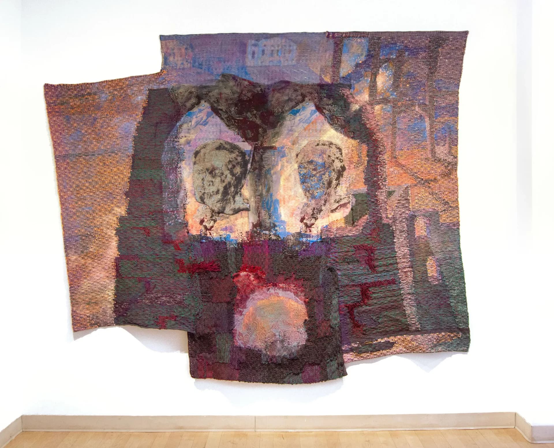 Layered textile wall installation with woven fabrics in earthy and jewel tones, featuring abstract faces and architectural elements, by Maris Van Vlack.