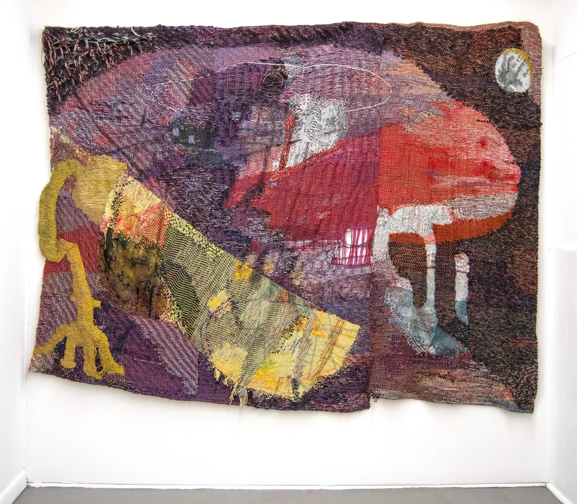 Textured fiber art wall hanging featuring abstract figures in purple, red, yellow, and brown tones with dimensional woven elements by Maris Van Vlack.