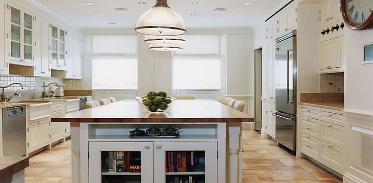 Bright, modern kitchen with white cabinetry, wood-topped island with open shelving, stainless steel appliances, and pendant lighting by Marjorie Hilton.