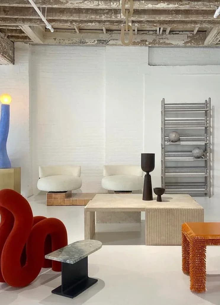 Contemporary interior showroom with cream curved seating, natural wood desk, metallic towel rack, and sculptural red organic furniture by Mark Malecki.