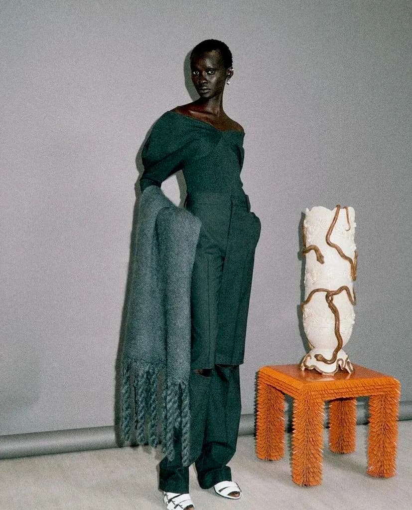 Fashion styling with model wearing teal knit ensemble and draped shawl, posed next to sculptural orange and cream textile furniture pieces by Mark Malecki.