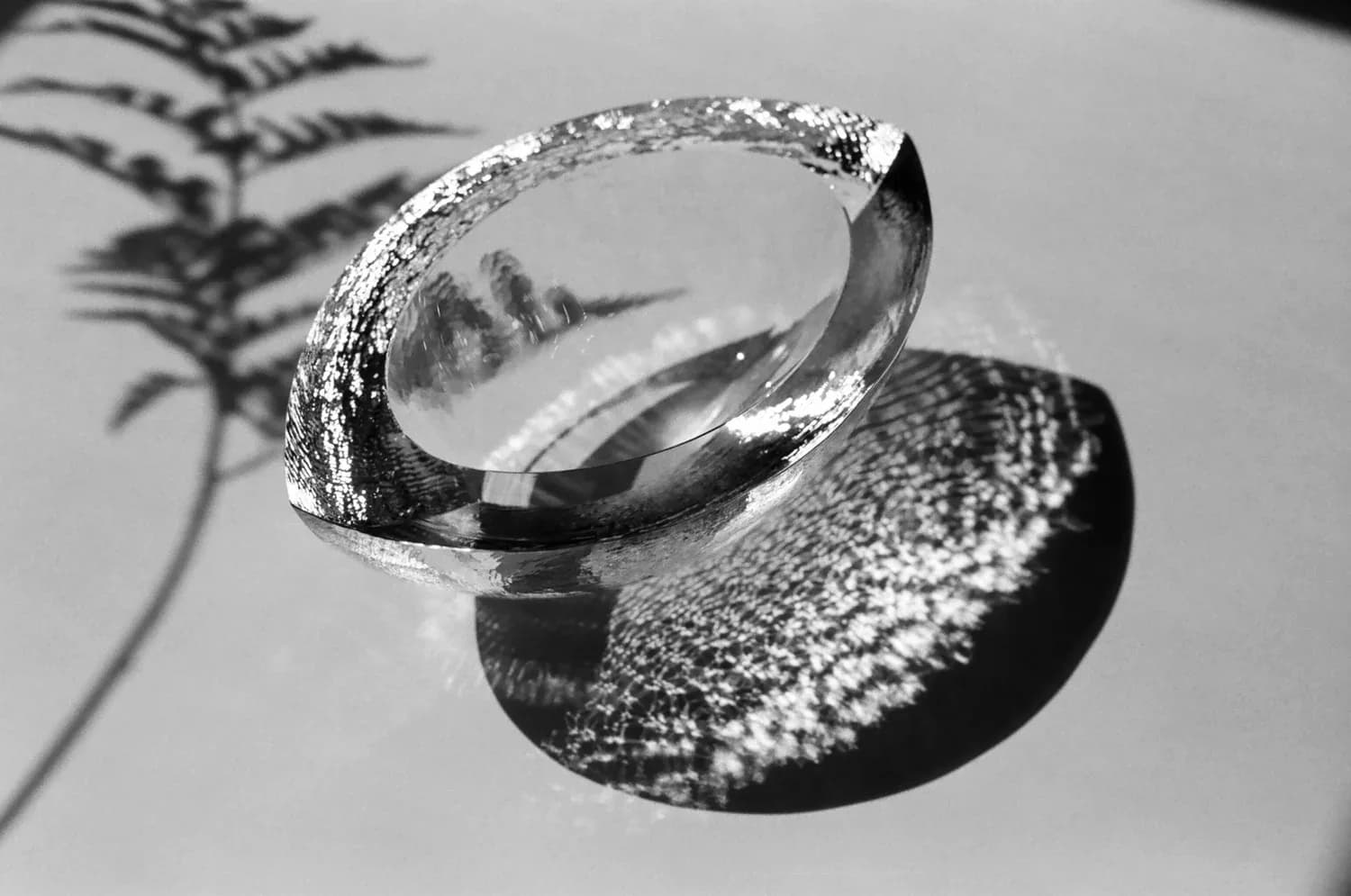 Artistic still-life photograph of textured silver bangles and jewelry casting dramatic shadows against a minimalist background by Mark Pavlovits.