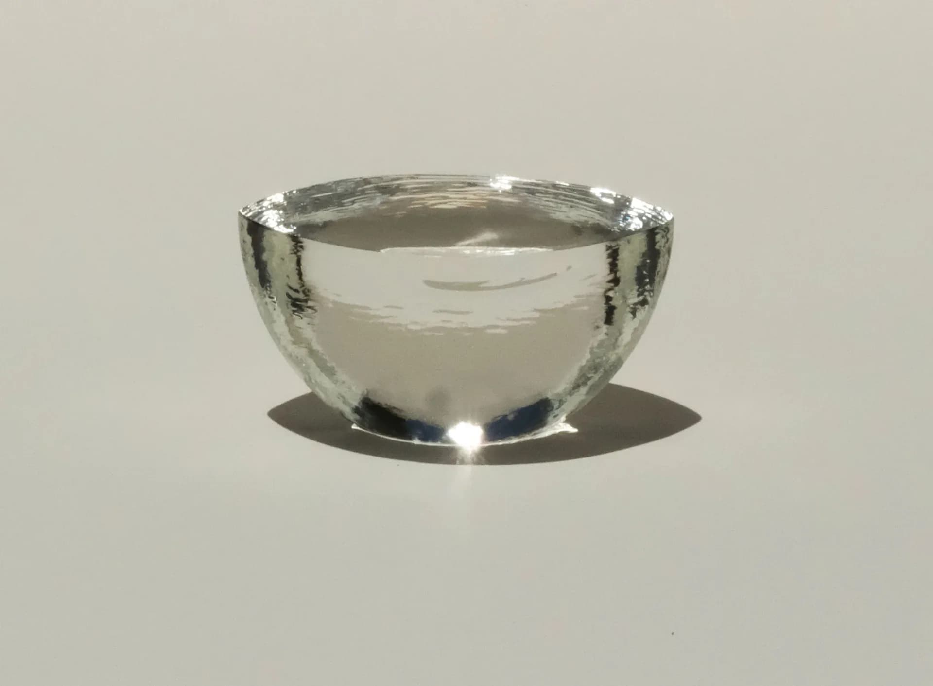 Polished stainless steel hemispherical bowl with reflective surface and dramatic lighting, casting shadow on neutral ground by Mark Pavlovits.