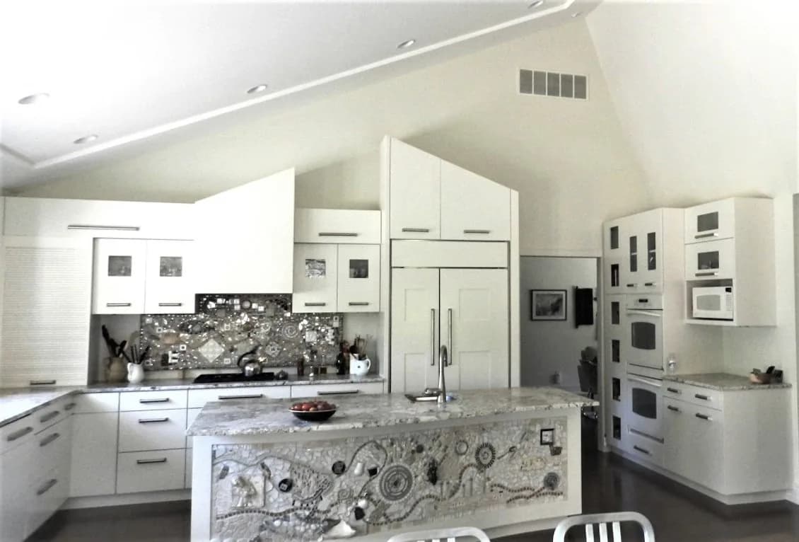 Modern white kitchen with geometric patterned island and backsplash, vaulted ceiling, and stainless steel appliances by Mark Rosenhaus.