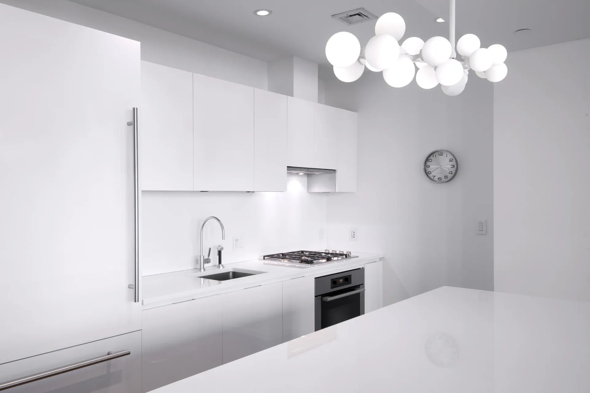Minimalist white kitchen with sleek cabinetry, integrated appliances, white quartz countertop, and modern pendant lighting by Marlene Bednarz.