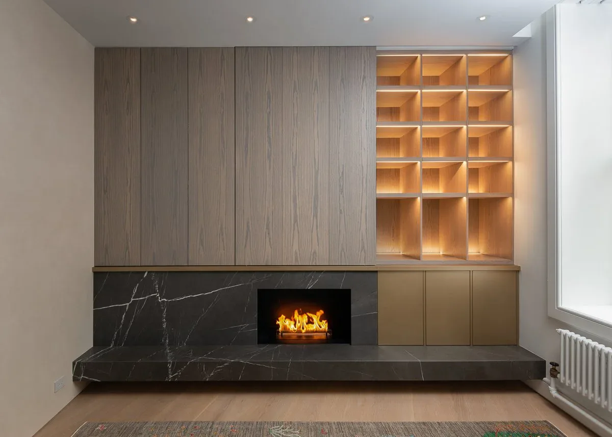 Contemporary living room with built-in fireplace, marble surround, and illuminated wooden shelving units flanking the hearth by Marlene Bednarz.