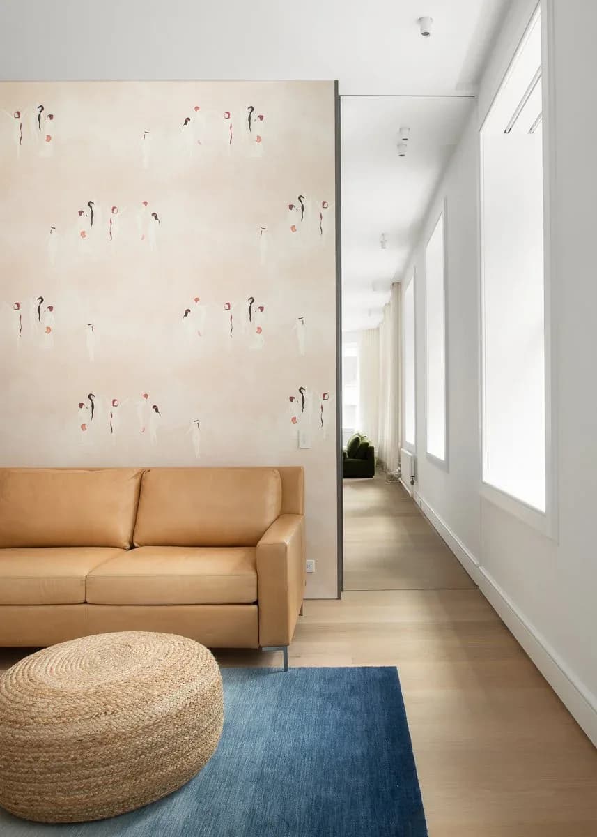 Modern living space with tan leather sofa, natural fiber pouf, blue area rug, and botanical wallpaper, designed by Marlene Bednarz.