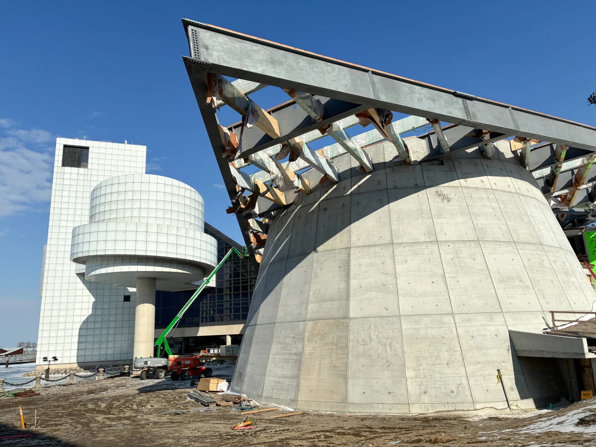 Brutalist concrete architectural structure with geometric curved forms and steel framework canopy under clear blue sky, by Mateo Fernández-Muro.