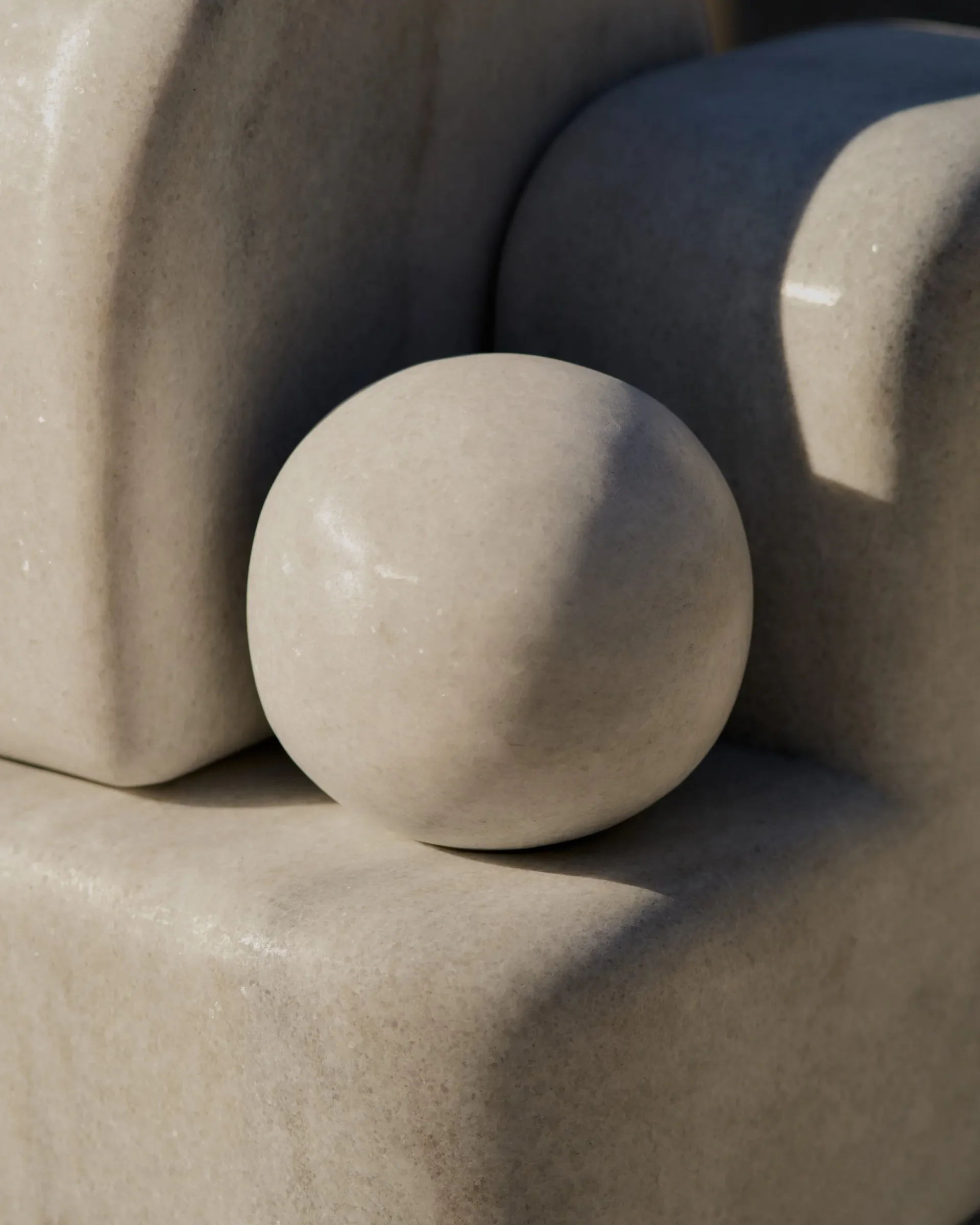 Minimalist sculptural composition featuring a pale sphere nestled between geometric stone forms, showcasing material and form study by Matthew Byrd.
