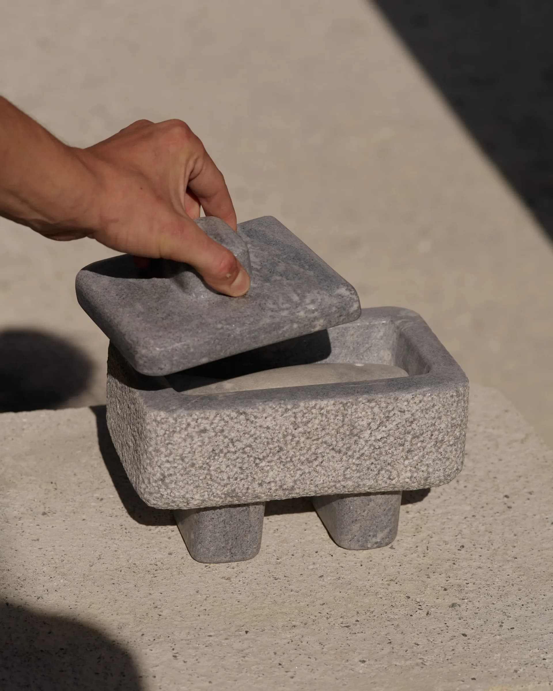 Hand holding a textured concrete sculptural object with angular geometric forms and a hollow interior cavity, by Matthew Byrd.