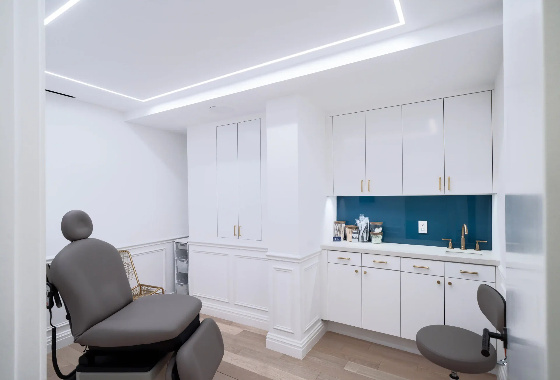 Modern dental operatory with white cabinetry, teal backsplash, clinical seating, and minimalist lighting design by Matthew Ruopoli.