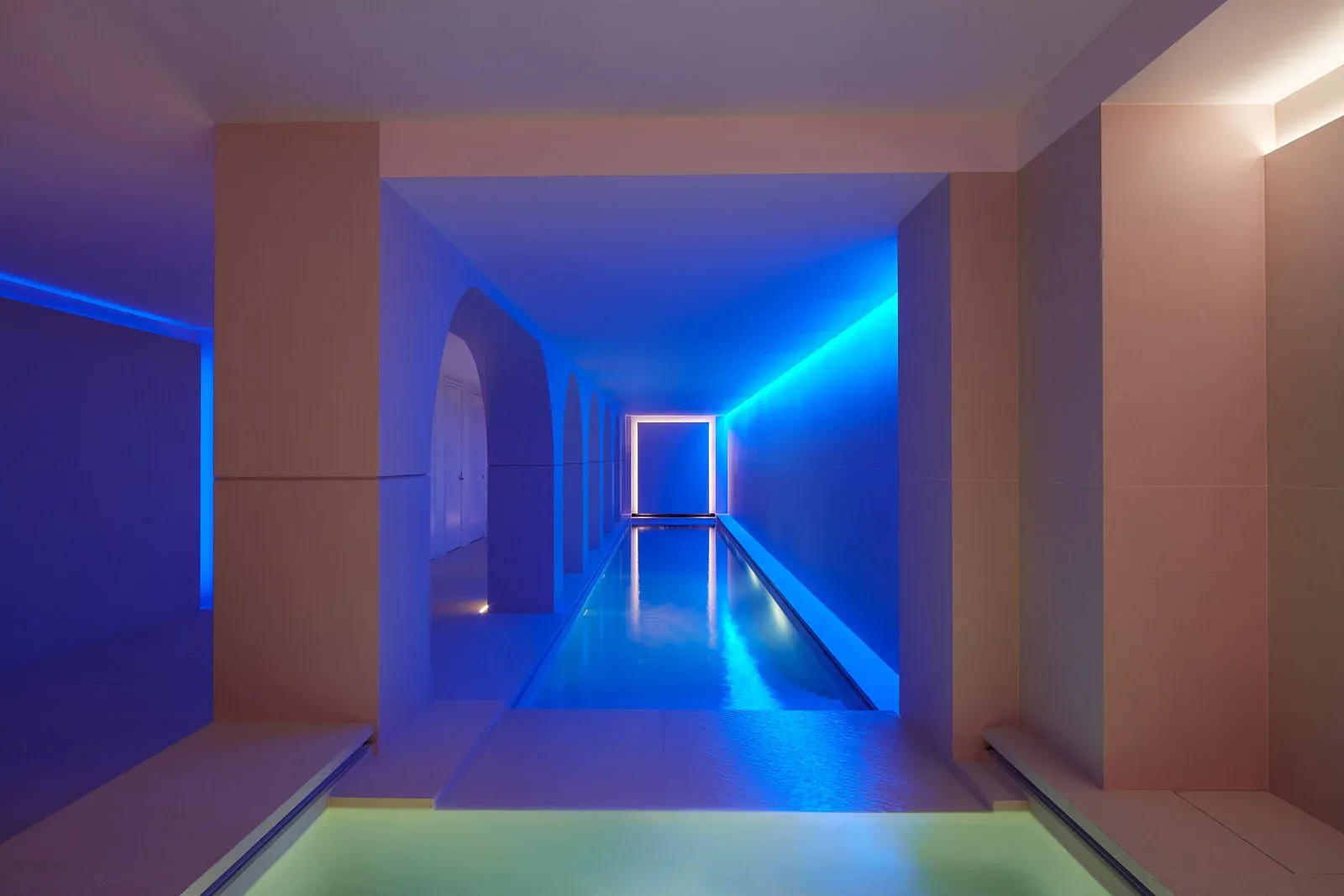 A neon-lit modern corridor with blue LED strip lighting, geometric architectural elements, and a minimalist aesthetic by Matthew Tirschwell.