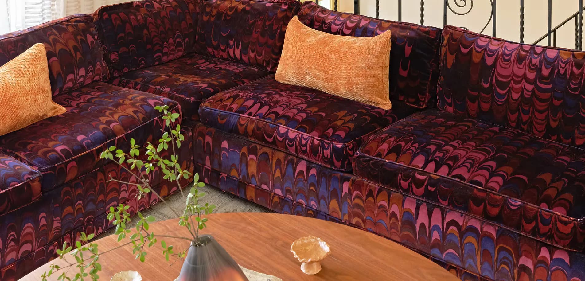 A burgundy sectional sofa with geometric patterning and gold accent pillows faces a wooden coffee table in a living room interior by Maura Clark.