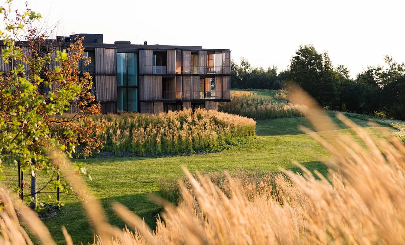 Modern dark-clad residential building set in rolling countryside with native grasses and green fields, architectural design by Maya Alawa.