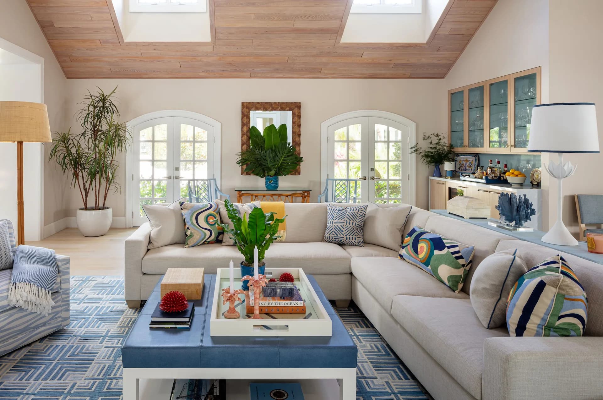 Bright coastal living room with beige sectional, blue and white geometric rug, skylight ceiling, arched windows, and fresh greenery throughout, by Meagan Maudsley.