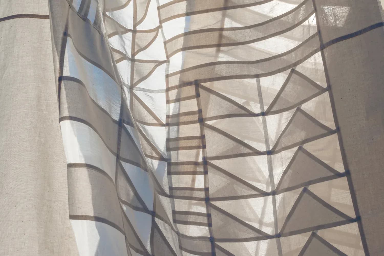 Layered sheer curtains with geometric triangle patterns create soft, filtered natural light in a contemporary interior by Meg Callahan.