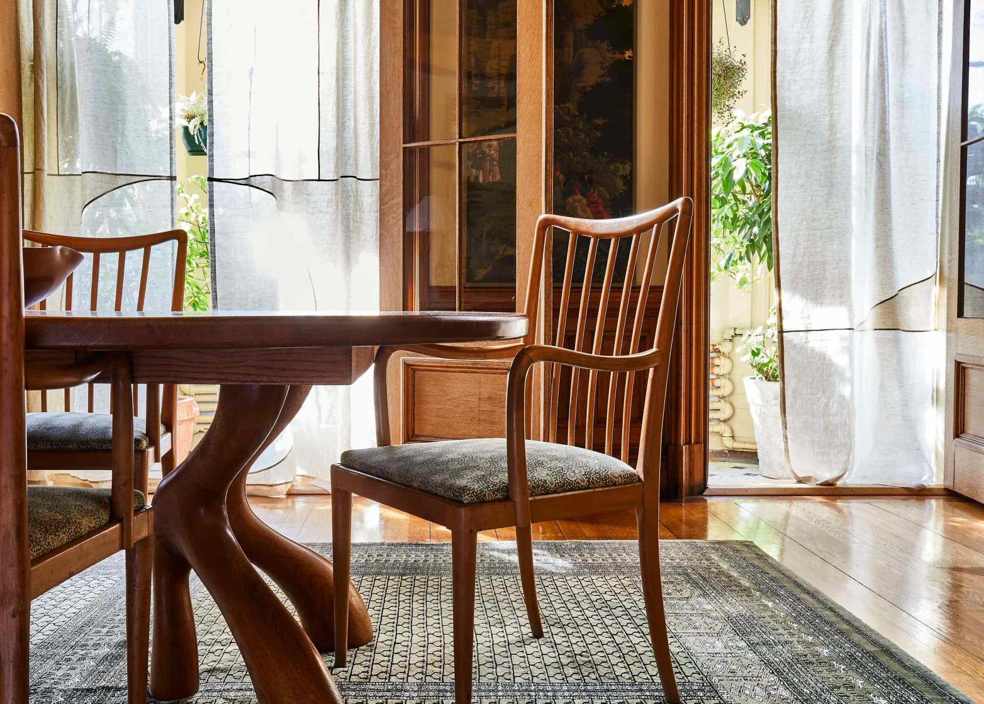 Dining room with mid-century modern wood table and chairs, natural light from glass doors, neutral palette with striped area rug by Meg Callahan.
