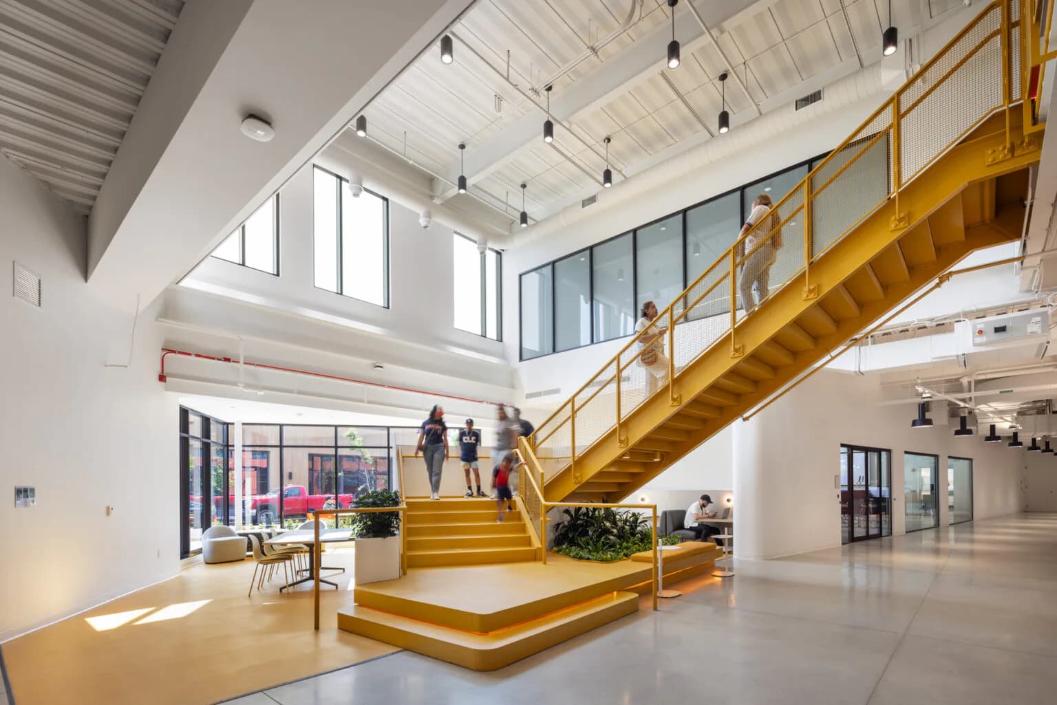 Bright, modern interior with a striking wooden staircase, high ceilings with skylights, polished concrete floors, and minimalist furnishings by Mel Casipit.