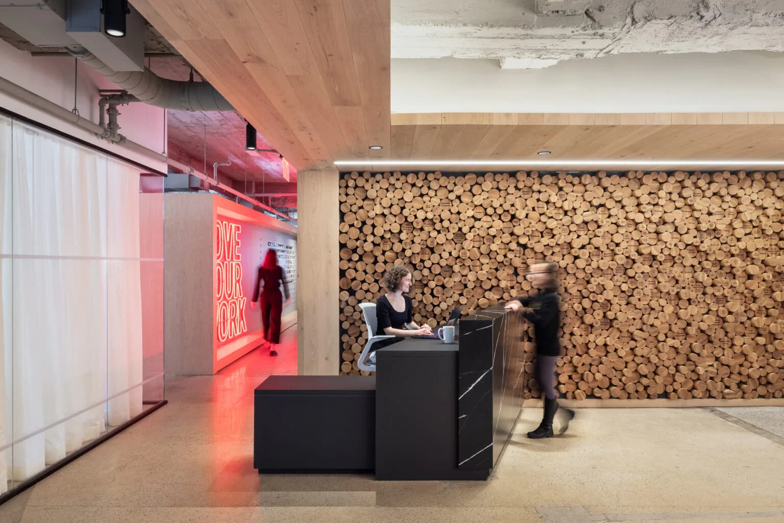 Modern commercial interior with cork wall installation, black reception desk, ambient red lighting, and concrete ceiling by Mel Casipit.