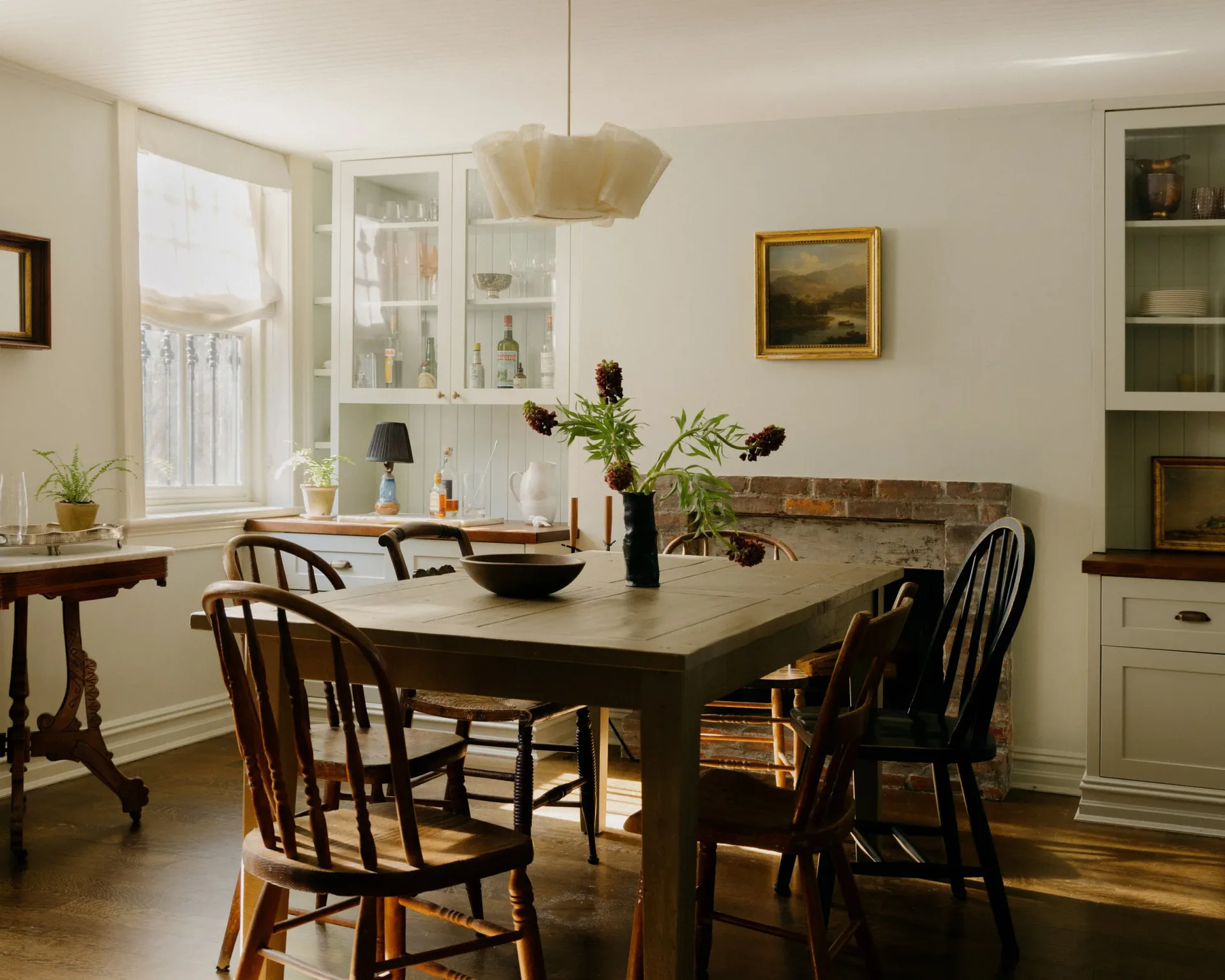 Dining room with dark wood table, Windsor chairs, pendant light fixture, built-in shelving, and large window by Melissa Lee.