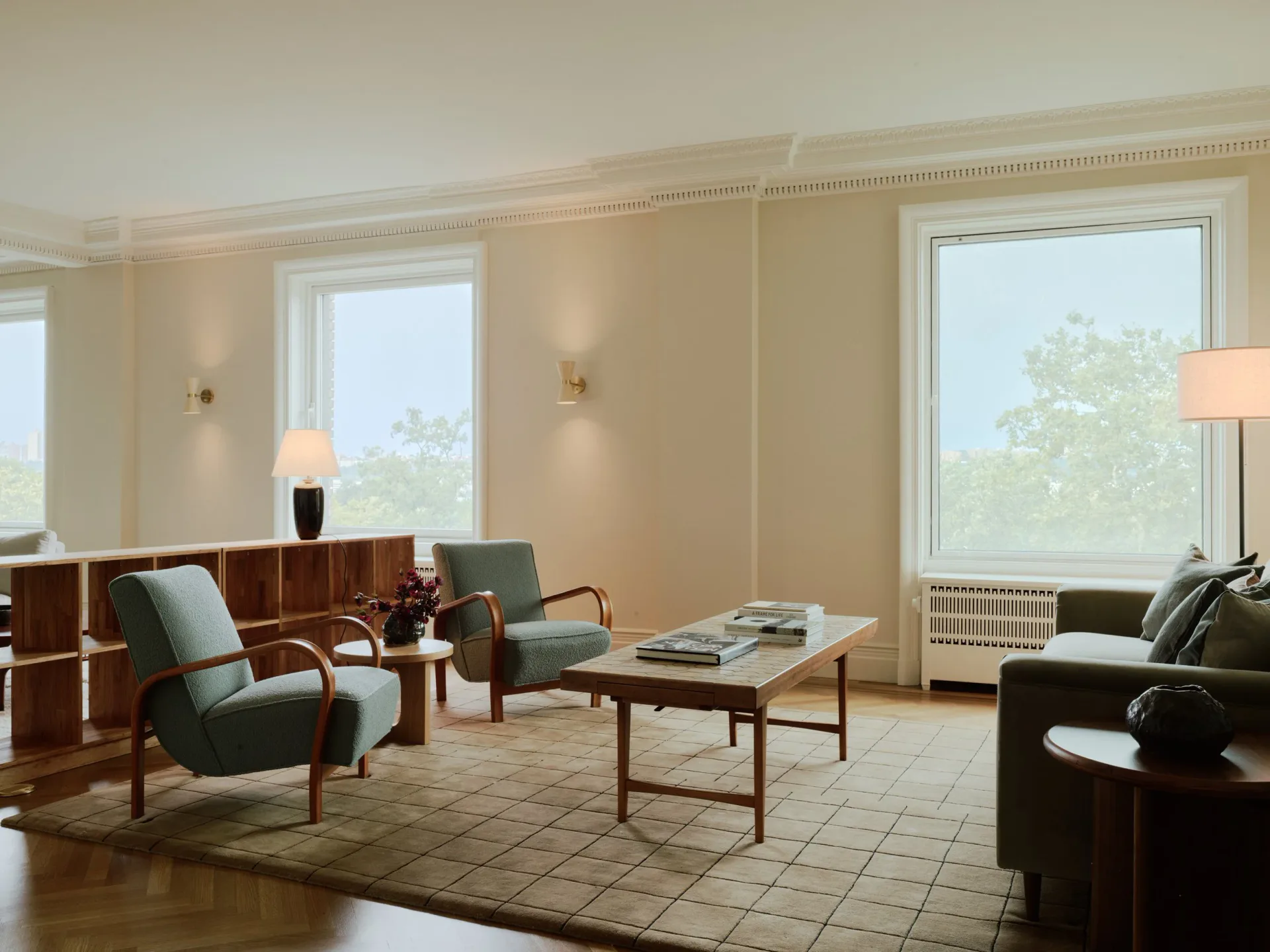 Bright modernist living room with mid-century furniture, large windows overlooking trees, neutral palette, and geometric area rug by Melissa Lee.