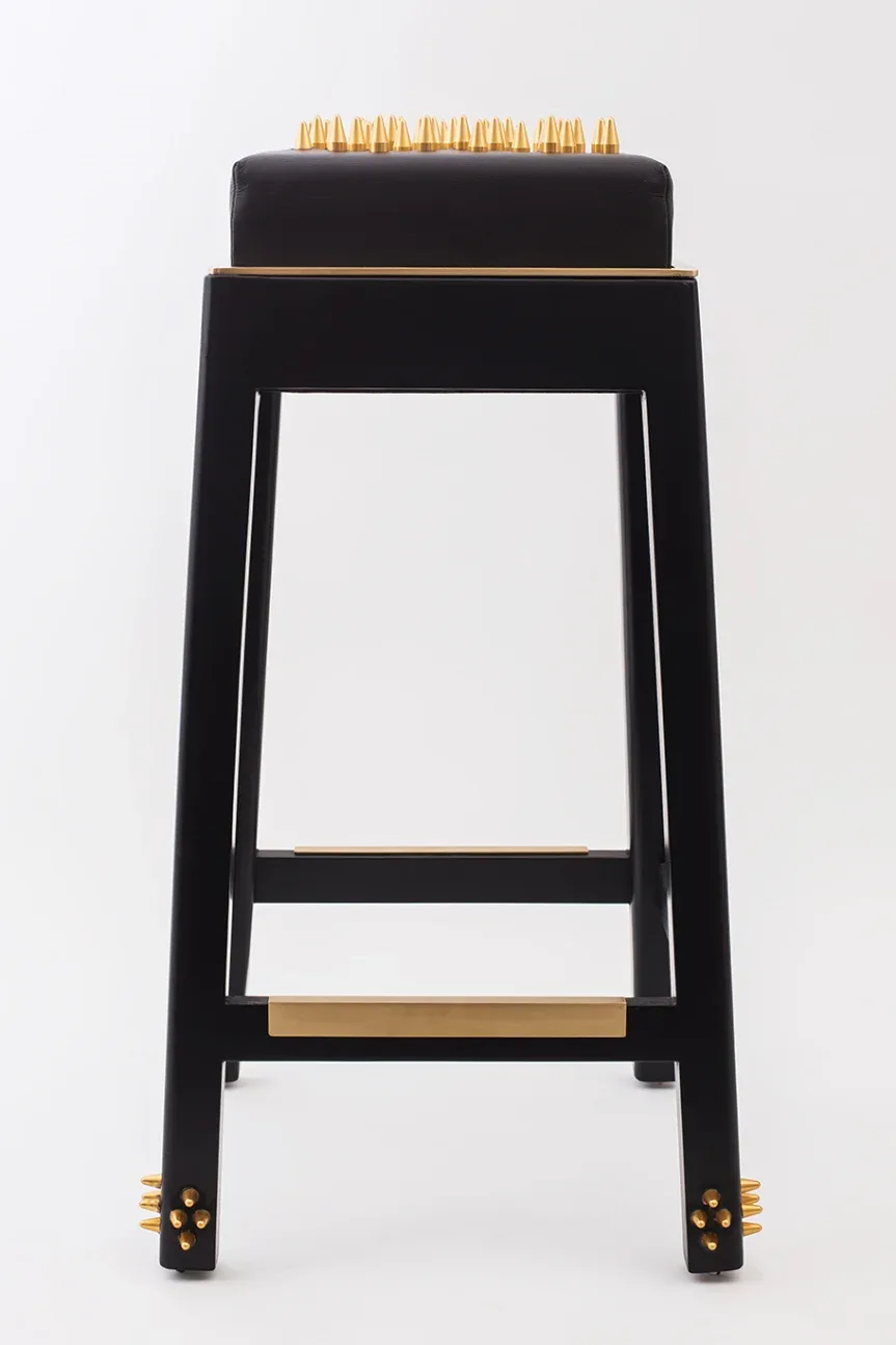 Black bar stool with brass accents and spiked details, featuring a padded seat with gold studs by Merve Kahraman.