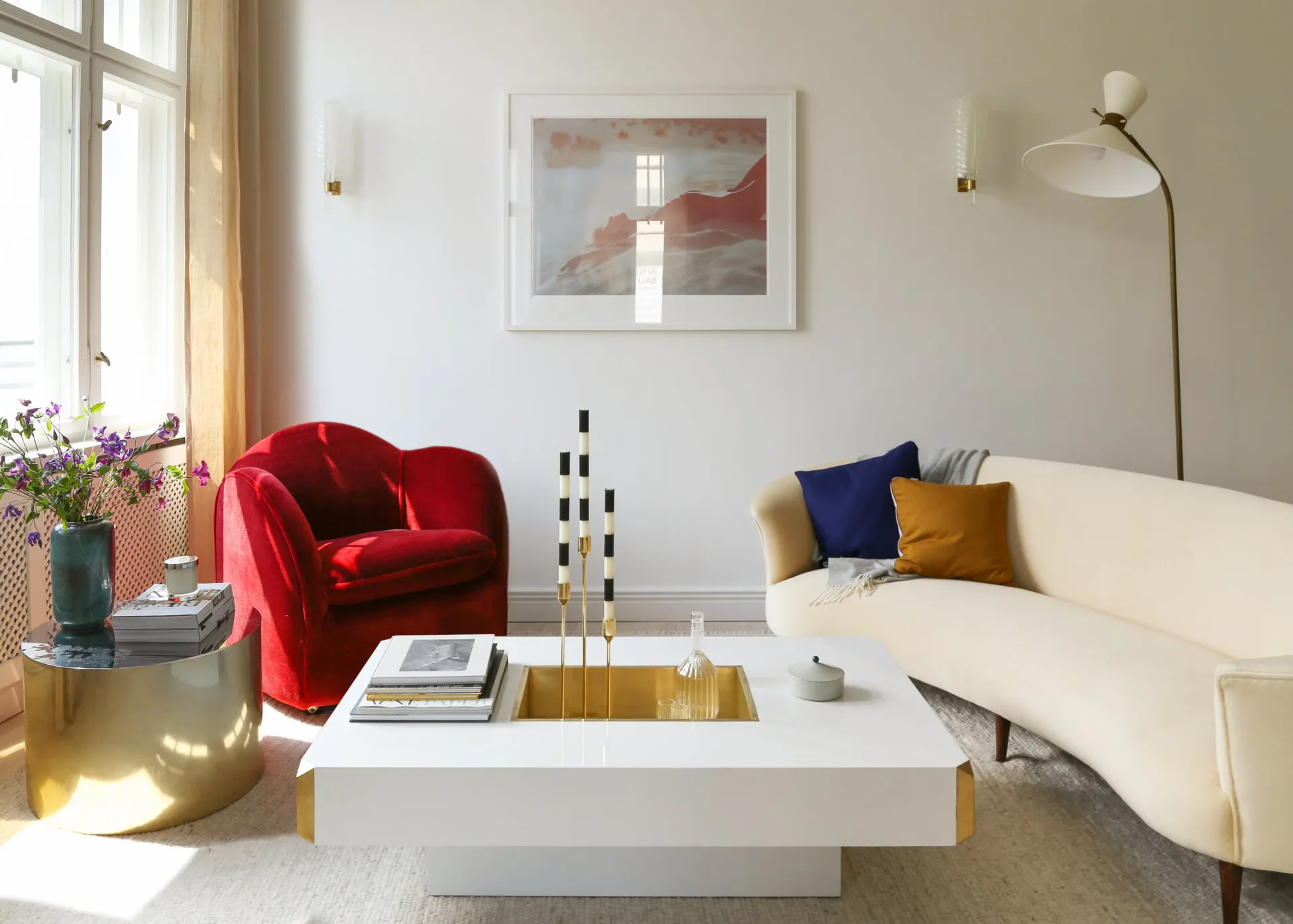 Contemporary living room with red velvet curved chair, cream sectional sofa, white coffee table, and warm natural lighting by Mia Jordan.