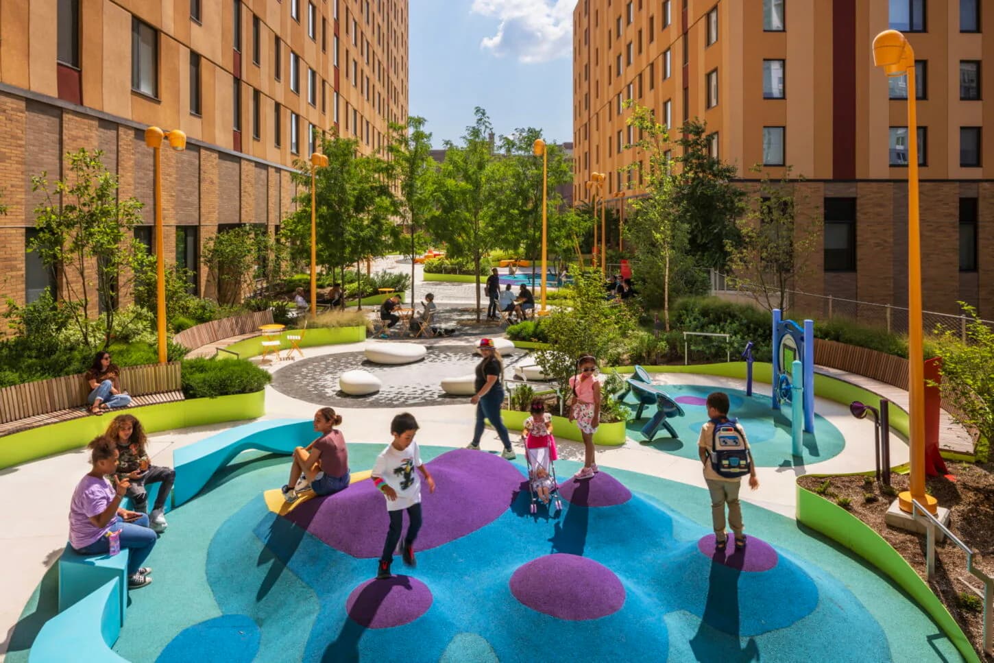 Vibrant courtyard playground with blue and purple sculptural elements, green lawn, and surrounding residential brick buildings by Michael Arad.