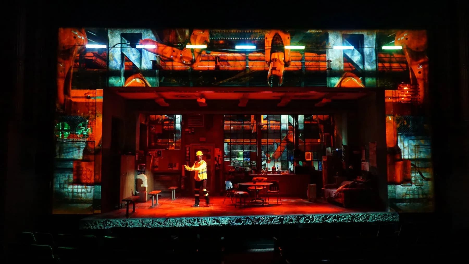 A vibrant theatrical stage set featuring warm red and orange lighting with teal accents, showcasing an interior environment designed by Michael Carnahan.