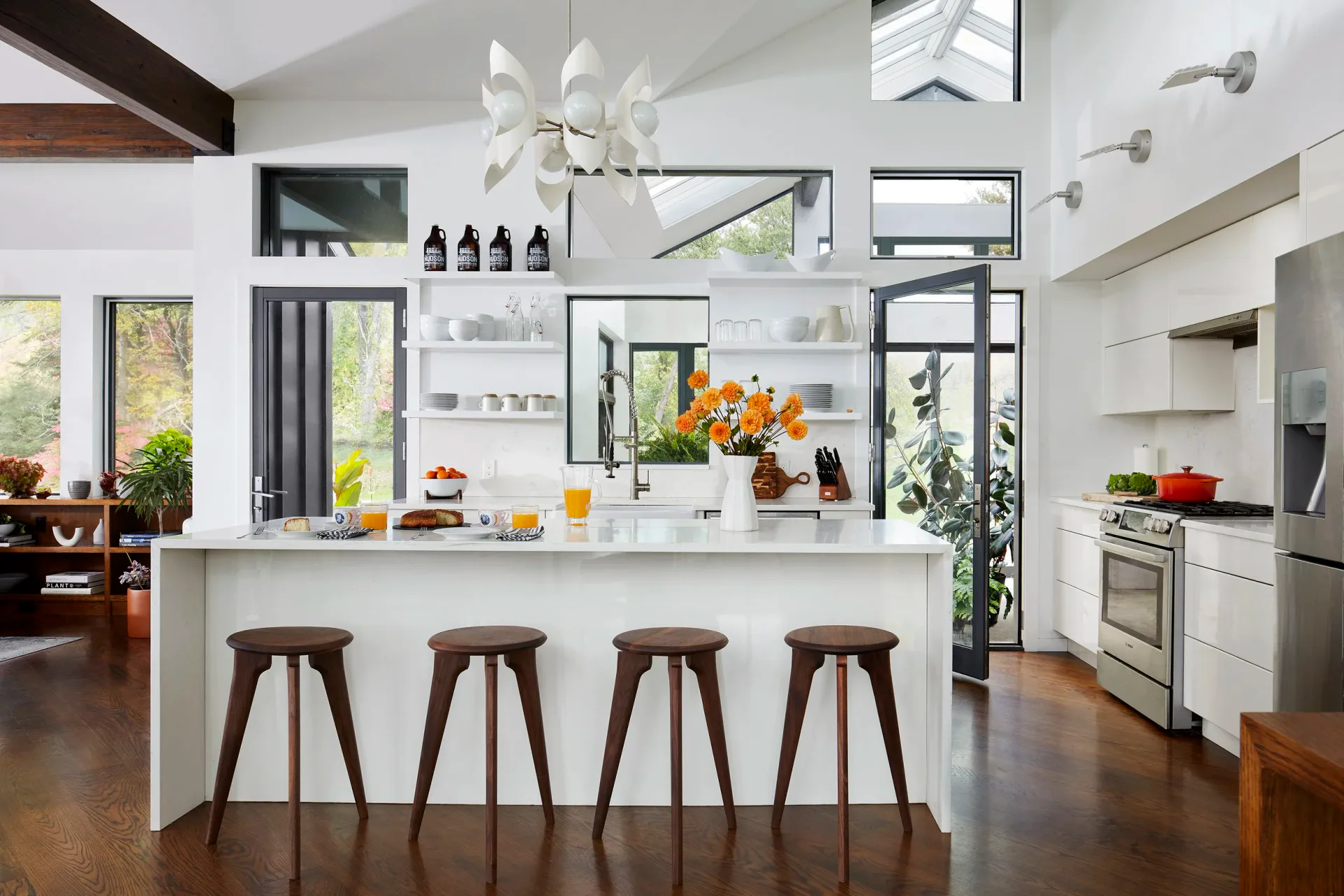 Contemporary kitchen with white cabinetry, waterfall island with four wooden stools, open shelving, and abundant natural light by Michael Gilbride.