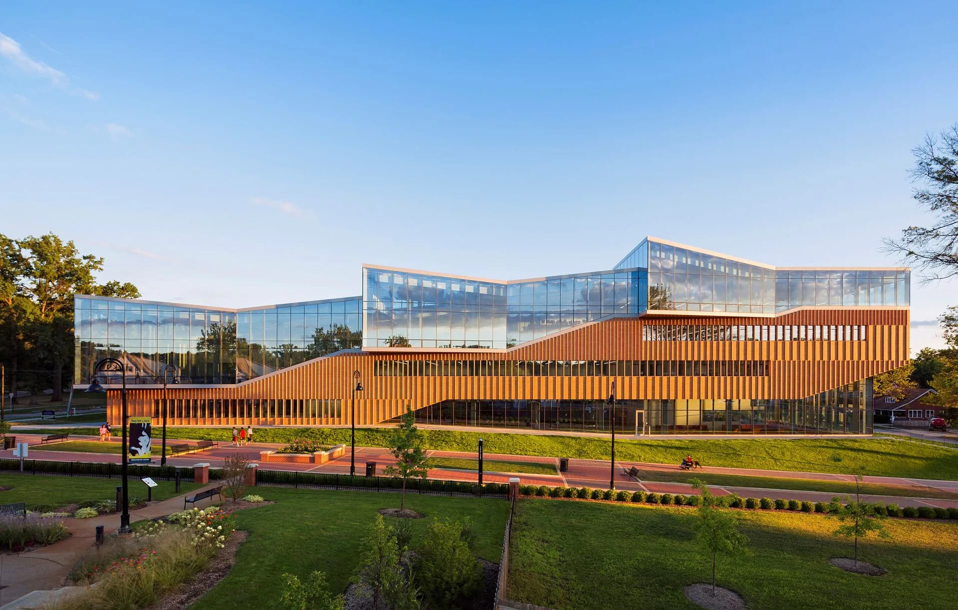 Modern institutional building with curved orange metal screening and glass upper levels overlooking a landscaped green space and waterway by Michael Manfredi.