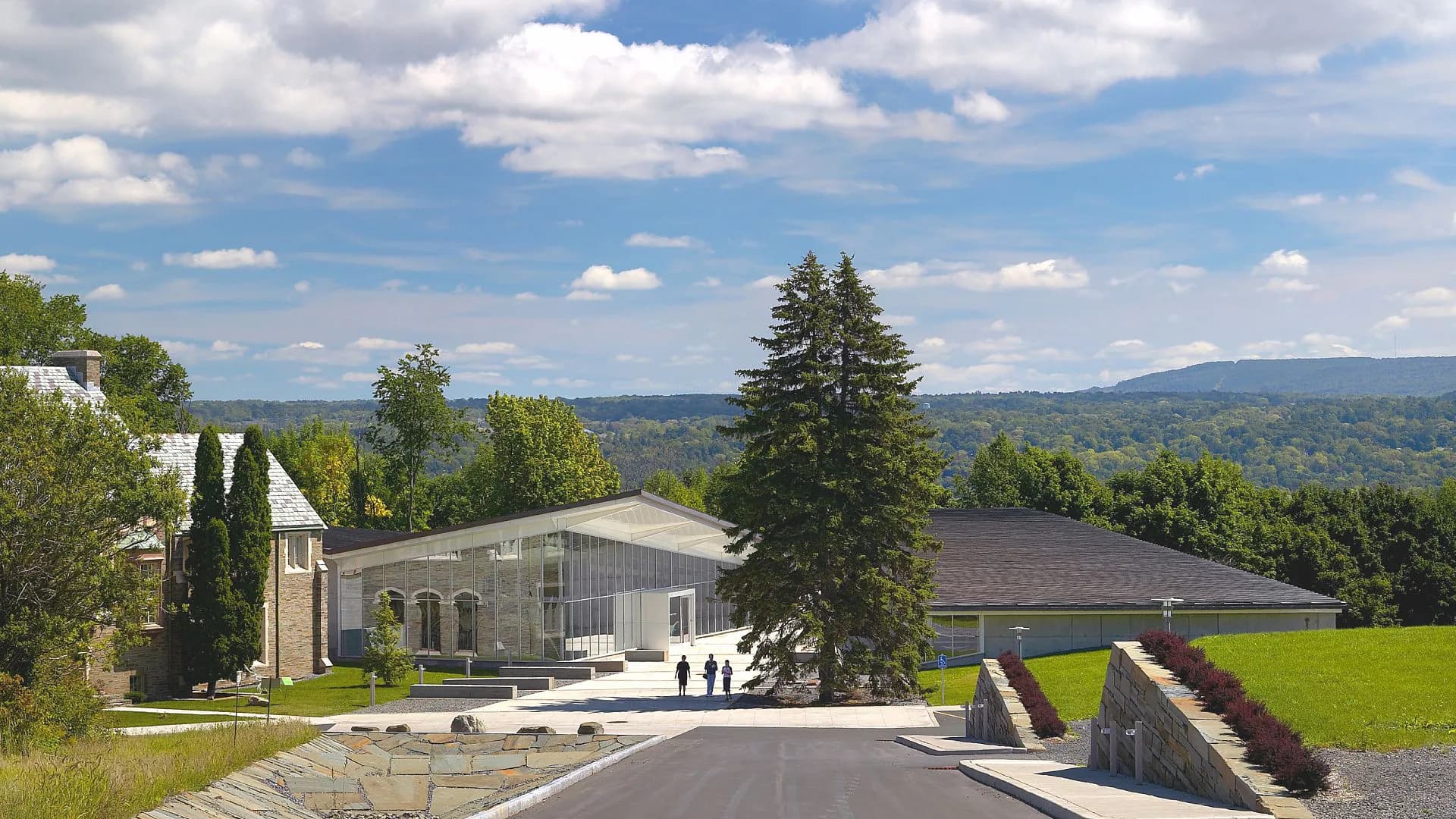 Modern residential building with curved glass and stone elements set on manicured grounds with distant mountains, by Michael Manfredi.