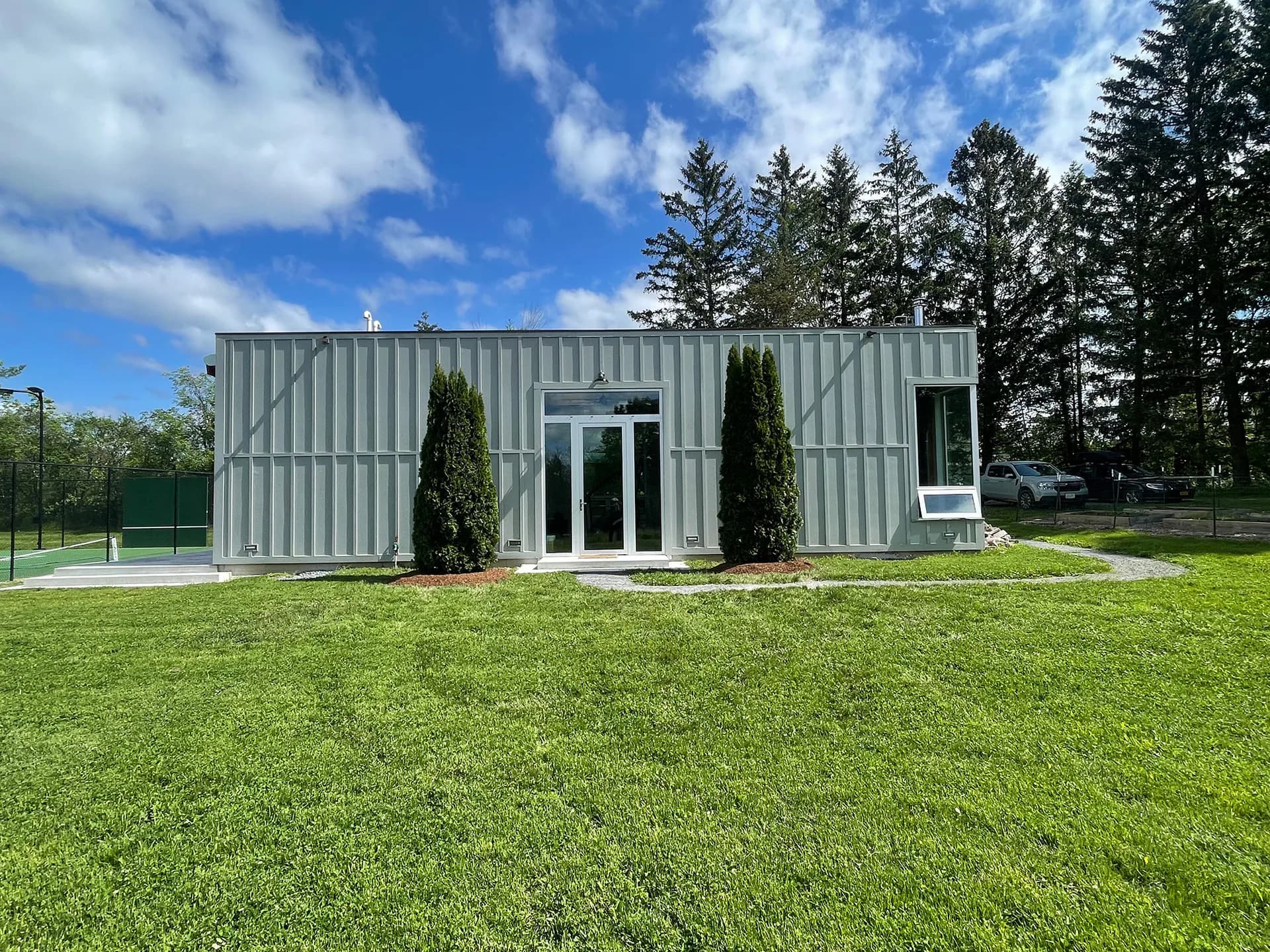Modern corrugated metal residential building with clean lines, flanked by evergreen trees, set on a manicured lawn by Michael Pierce.
