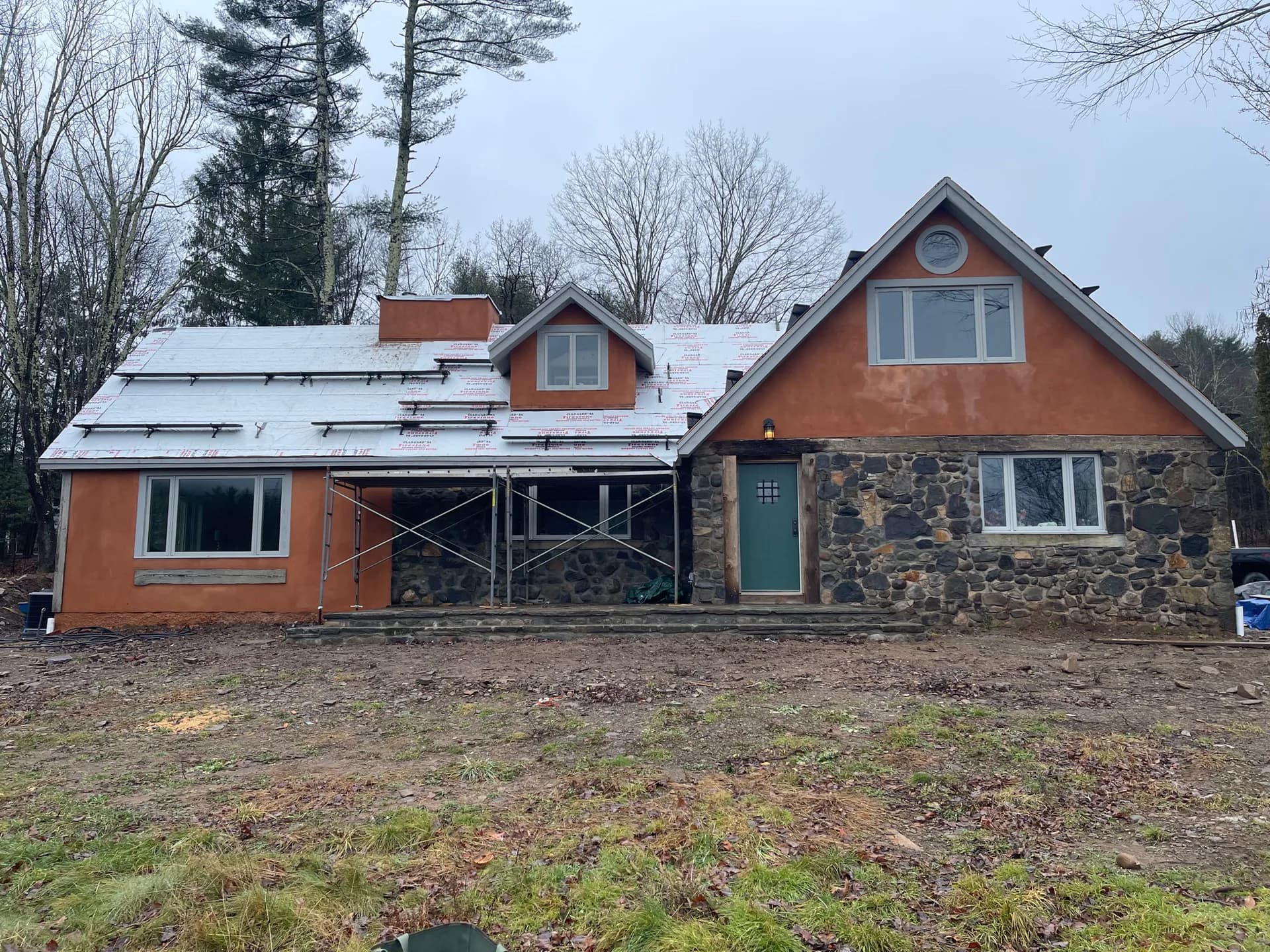 Modern residential home renovation with orange brick and stone exterior, featuring metal roofing and large windows, designed by Michael Pierce.