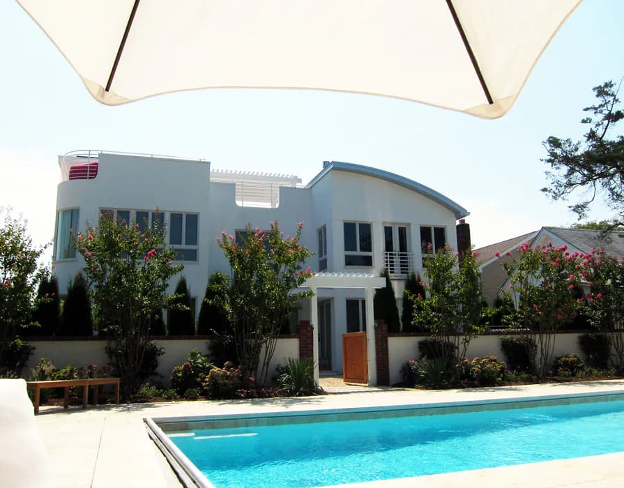 Modern two-story blue and white residential house with curved roofline, featuring a swimming pool in foreground and landscaped courtyard by Michael Pierce.