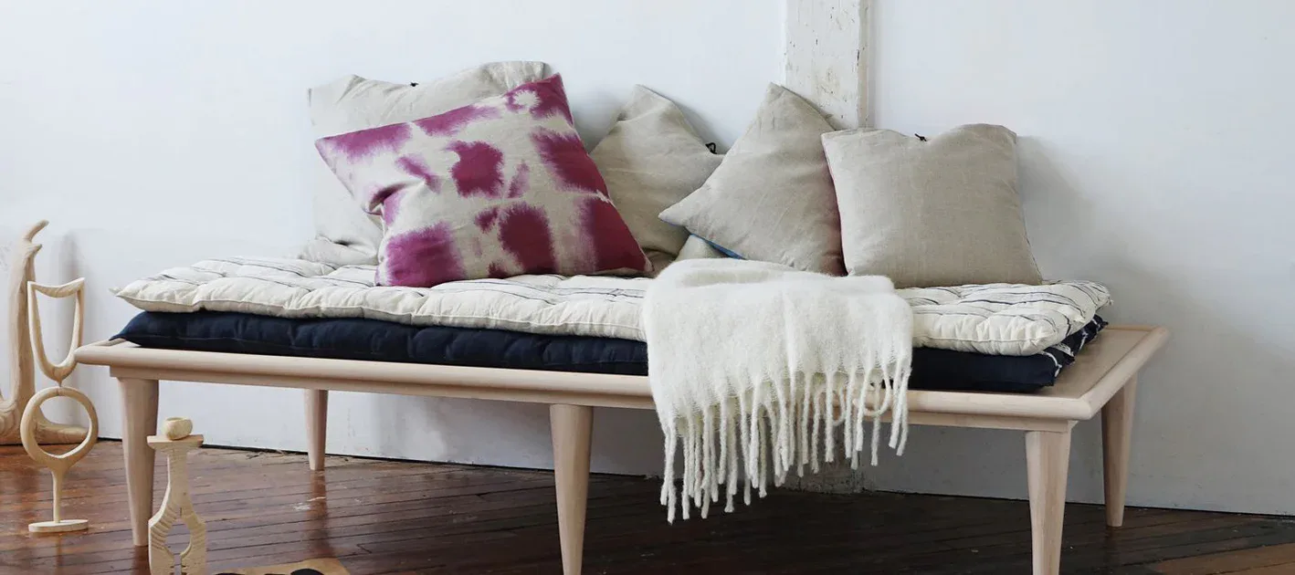 Light wood bench with black cushion topped with layered cream and patterned pillows and a fringed throw, styled interior by Michele Varian.