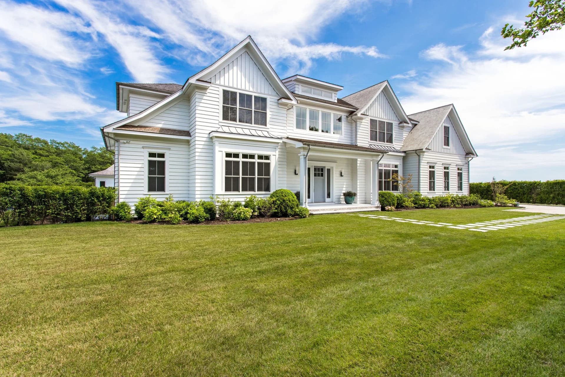 Modern white farmhouse with gabled roofline and large windows overlooks manicured lawn and landscaping by Michelle Breskin.