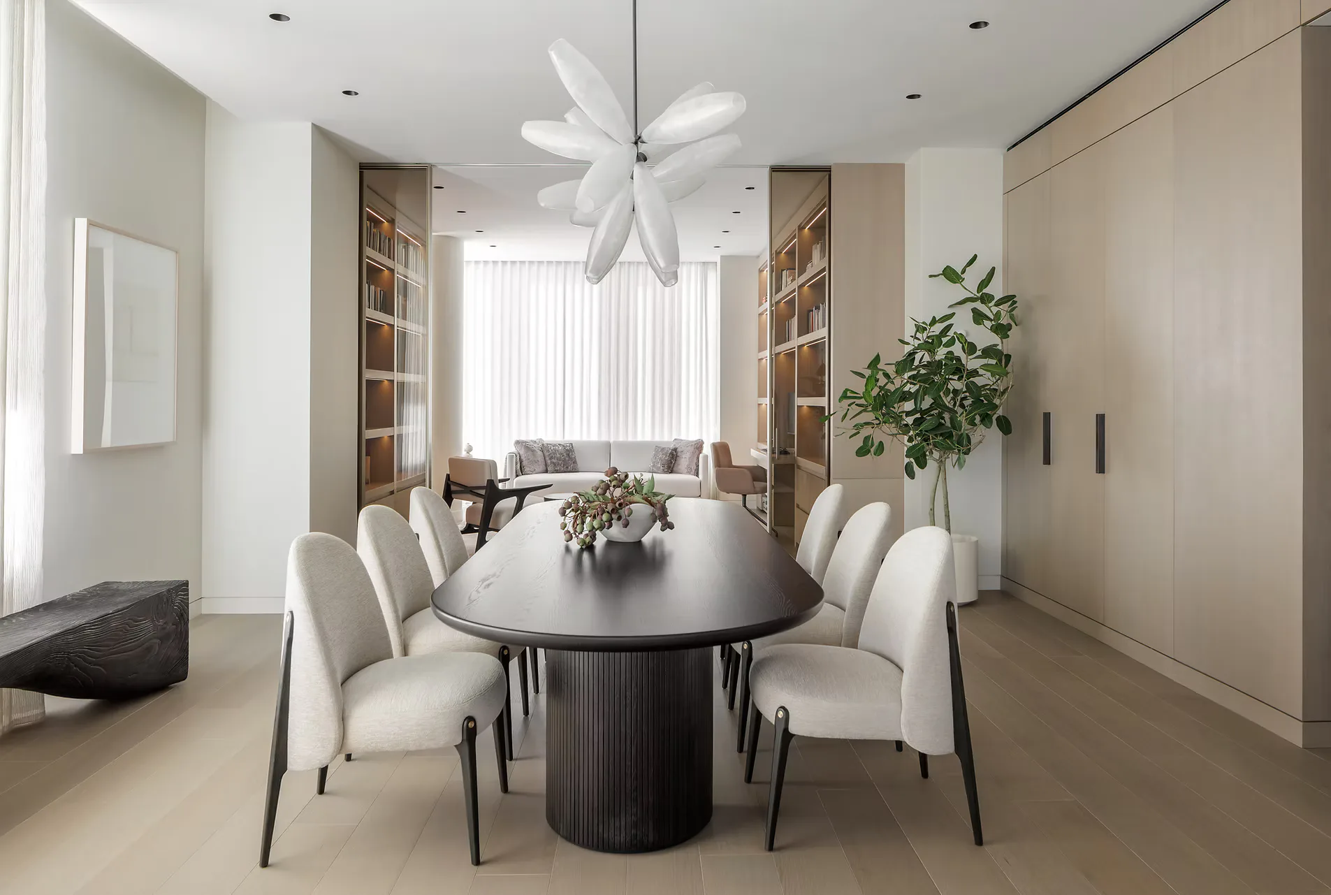 Modern dining room with oval black table, cream upholstered chairs, white flower pendant light, built-in shelving, and neutral palette by Michelle Pereira.