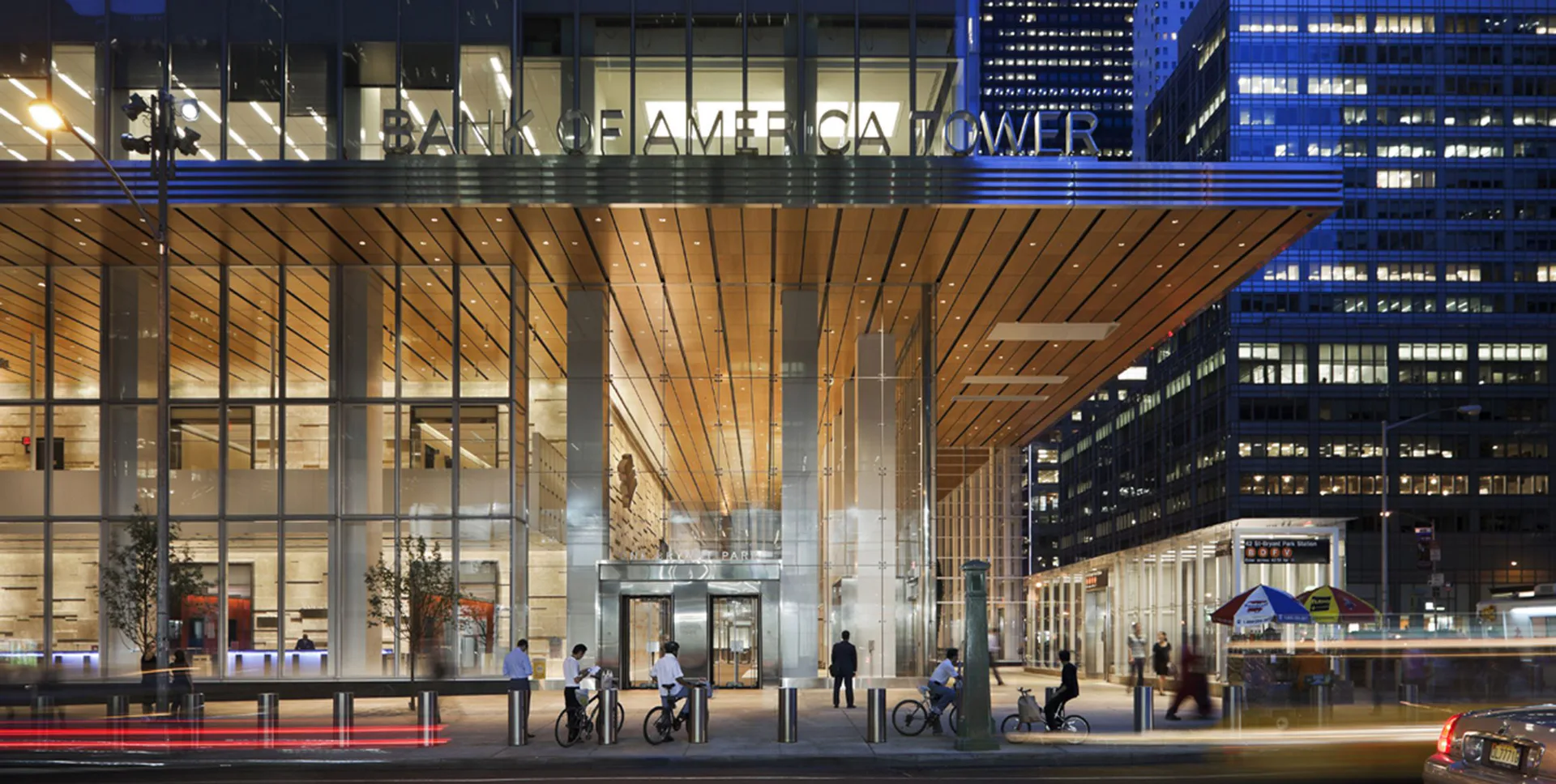 Modern high-rise lobby with floor-to-ceiling glazing, warm wood ceiling slats, polished stone flooring, and animated pedestrians in a nighttime urban setting by Michelle Romano.