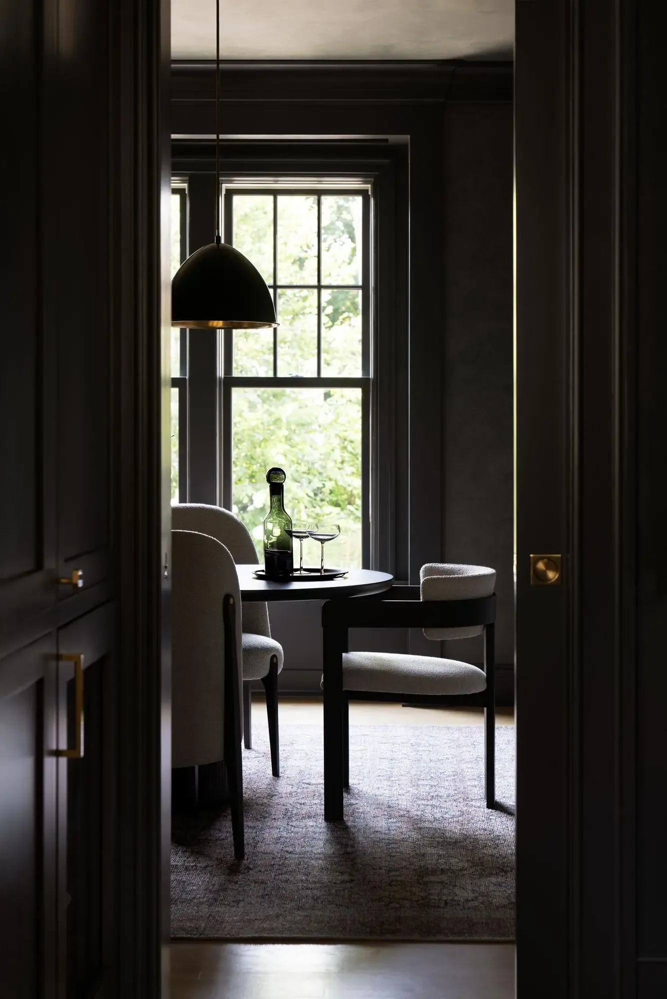 Dark moody study with black walls, pendant lamp, and large gridded window overlooking greenery, designed by Michelle Waugh.