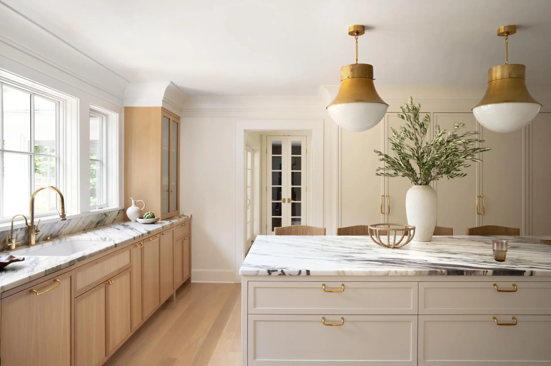 Bright kitchen with natural wood cabinetry, white island with brass hardware, brass pendant lights, and marble countertops designed by Michelle Waugh.