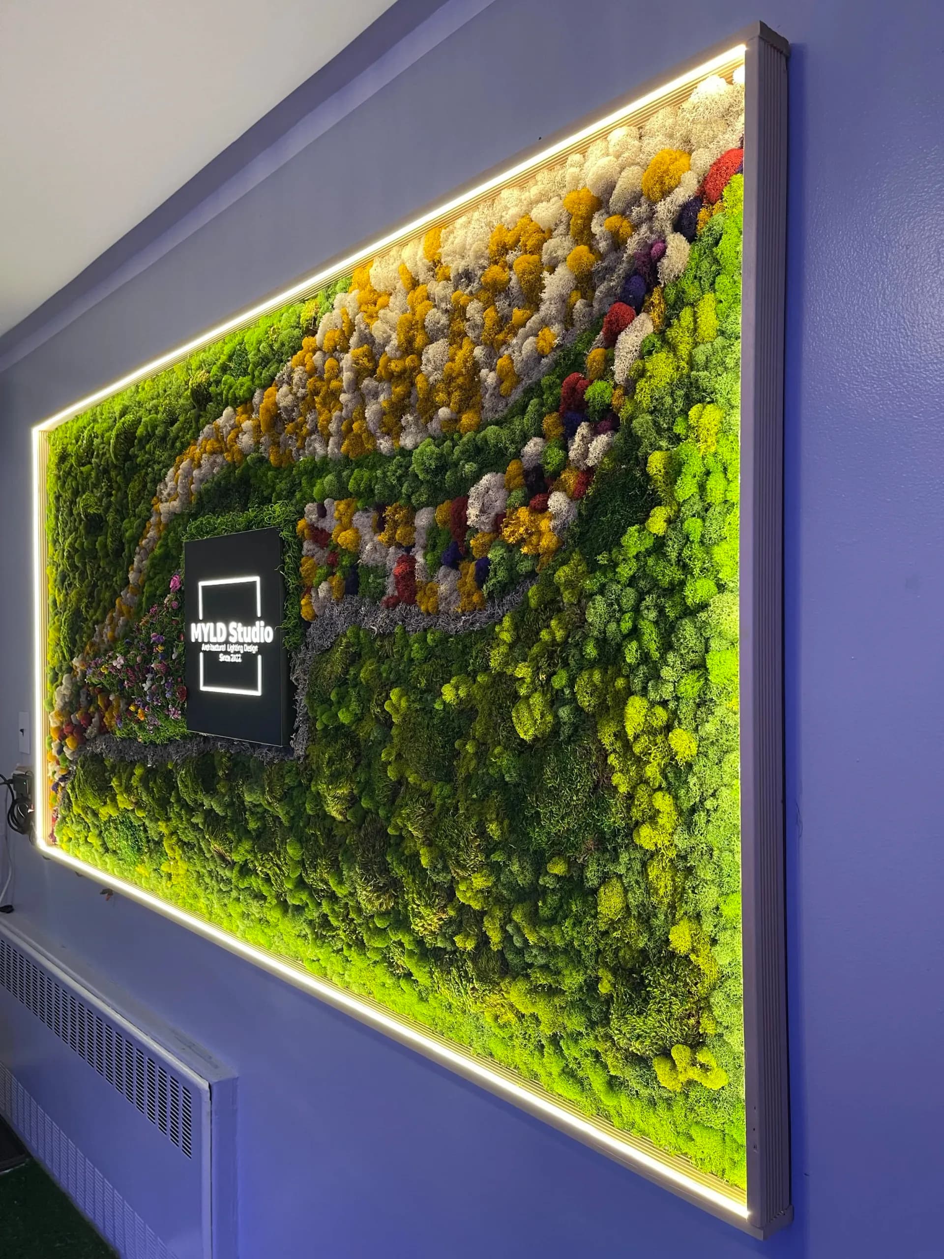 Living moss and flower wall installation with integrated LED lighting and branding element, featuring vibrant green and yellow tones by Michelle Yang.