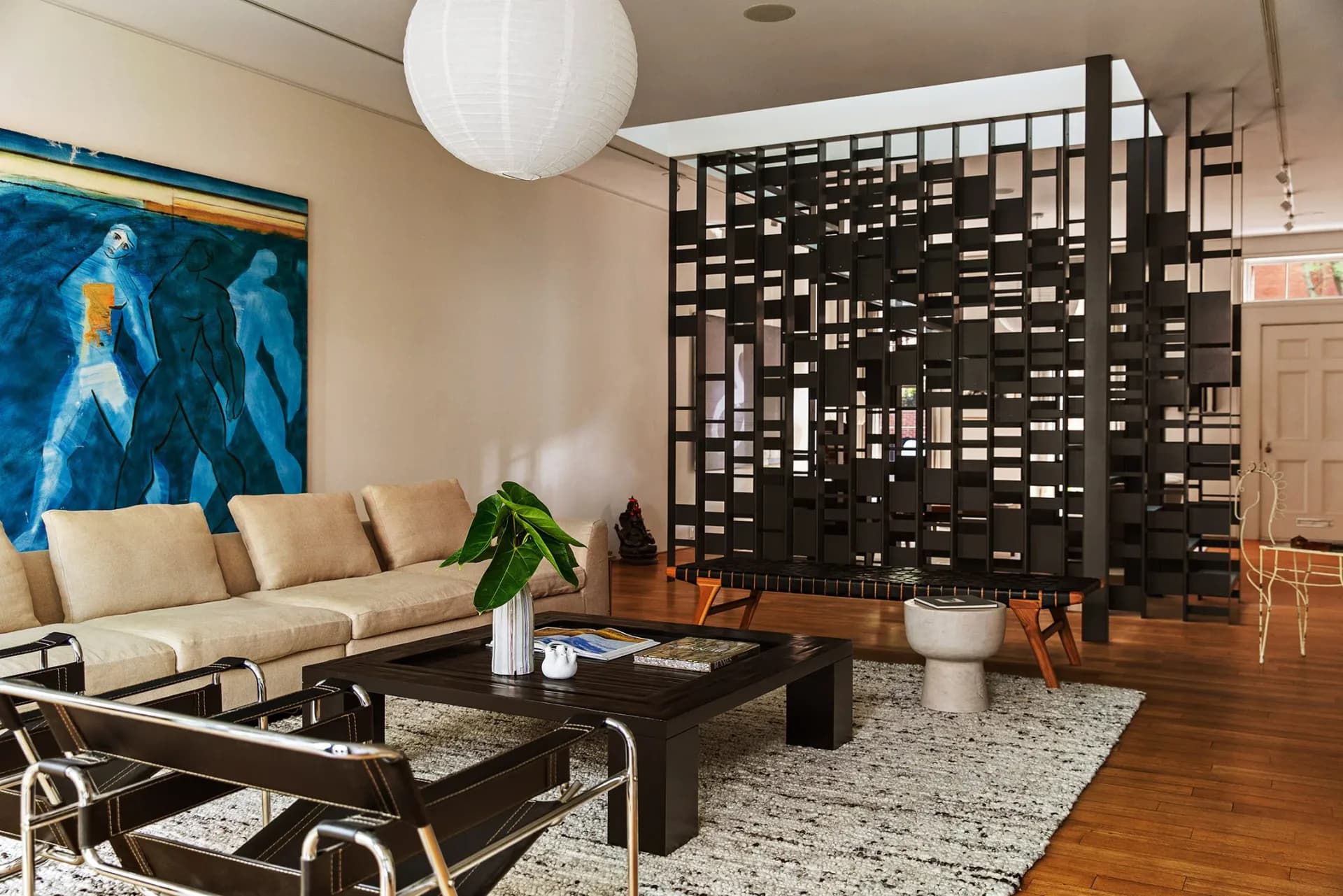 Contemporary living room with cream sectional, black coffee table, geometric room divider, and blue abstract artwork, designed by Mika Lipson.