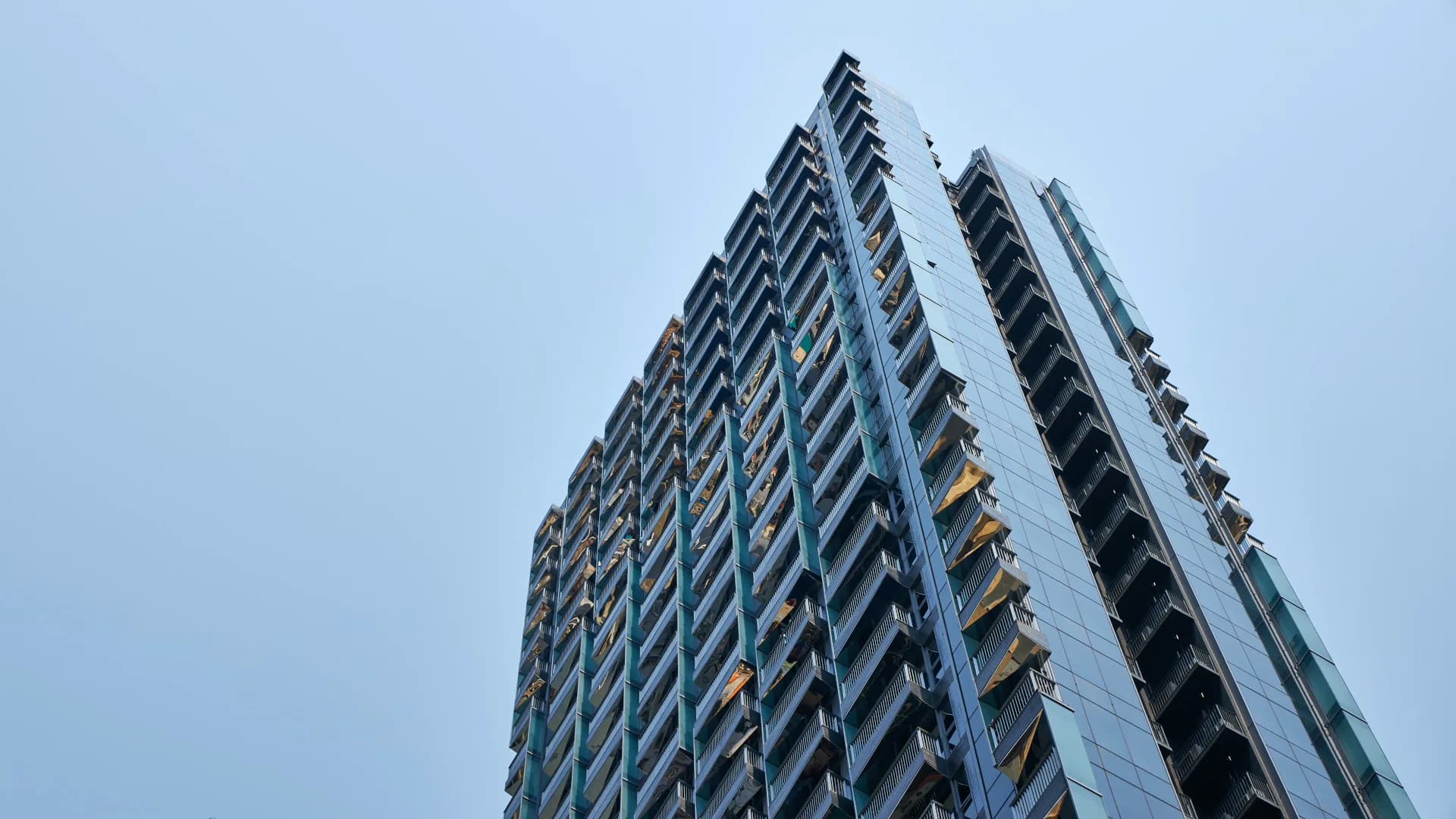 Tall residential tower with diagonal window patterns and geometric facade against blue sky, designed by Mimi Hoang.