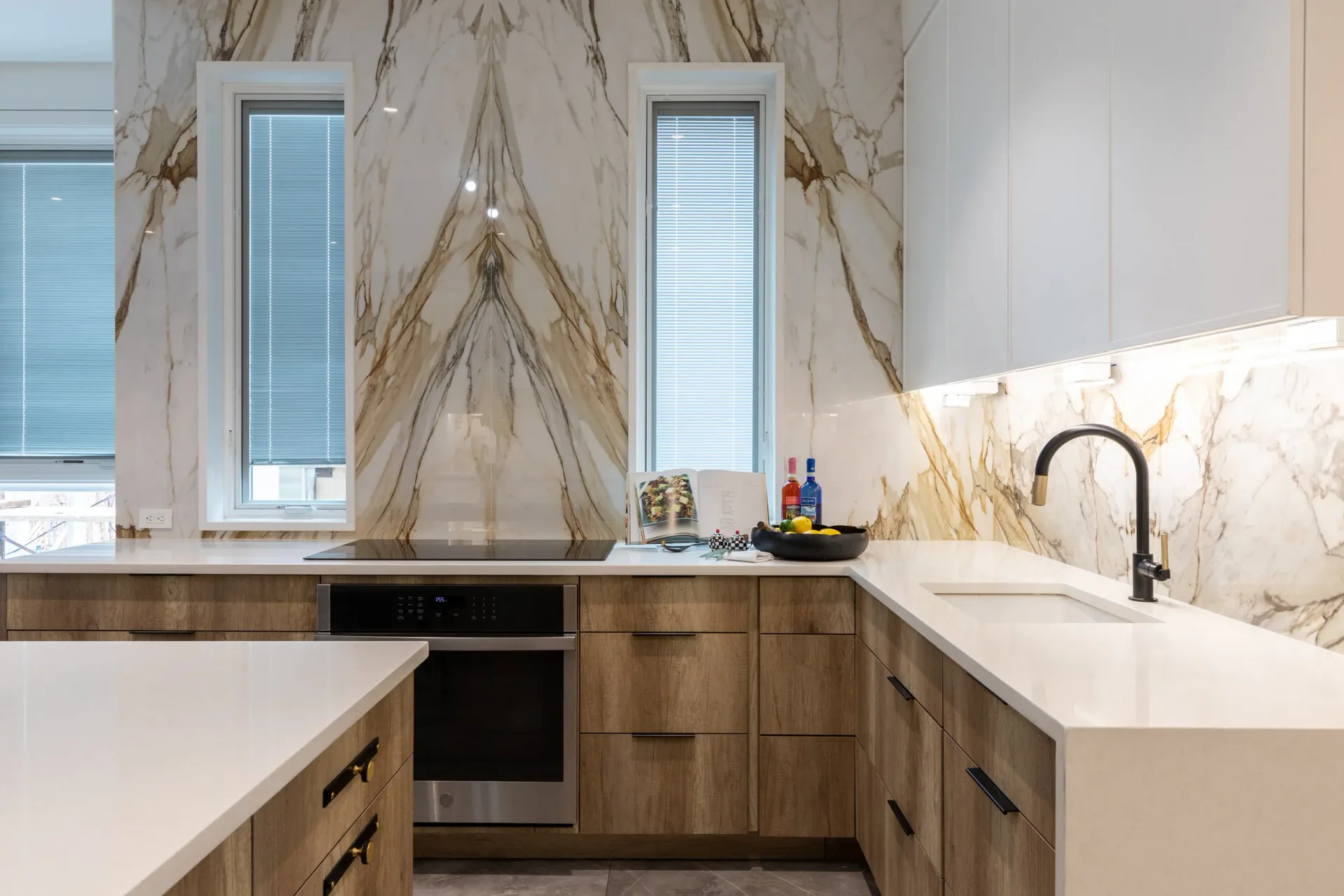Modern kitchen with symmetrical marble backsplash, white countertops, natural wood cabinetry, and black fixtures designed by Miriam Lichtenstein.